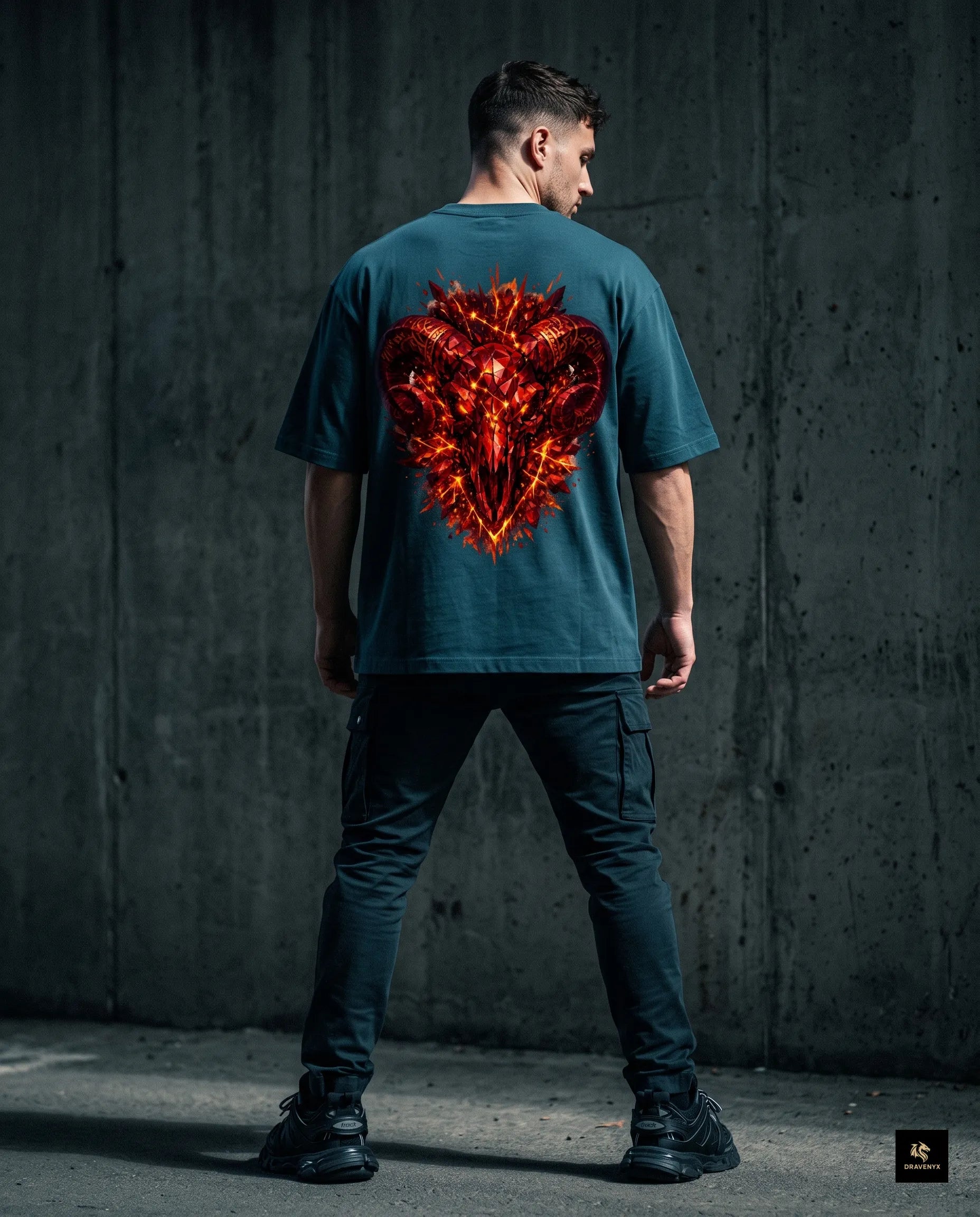 DRAVENYX® Aries Infernal Ram Oversized Tee in Petrol Blue — front view featuring left-chest crystalline Aries wing-mark emblem in molten amber and iron tones — back view showing full DTF print of infernal crystal ram skull with rune-inscribed curling horns and golden ember burst