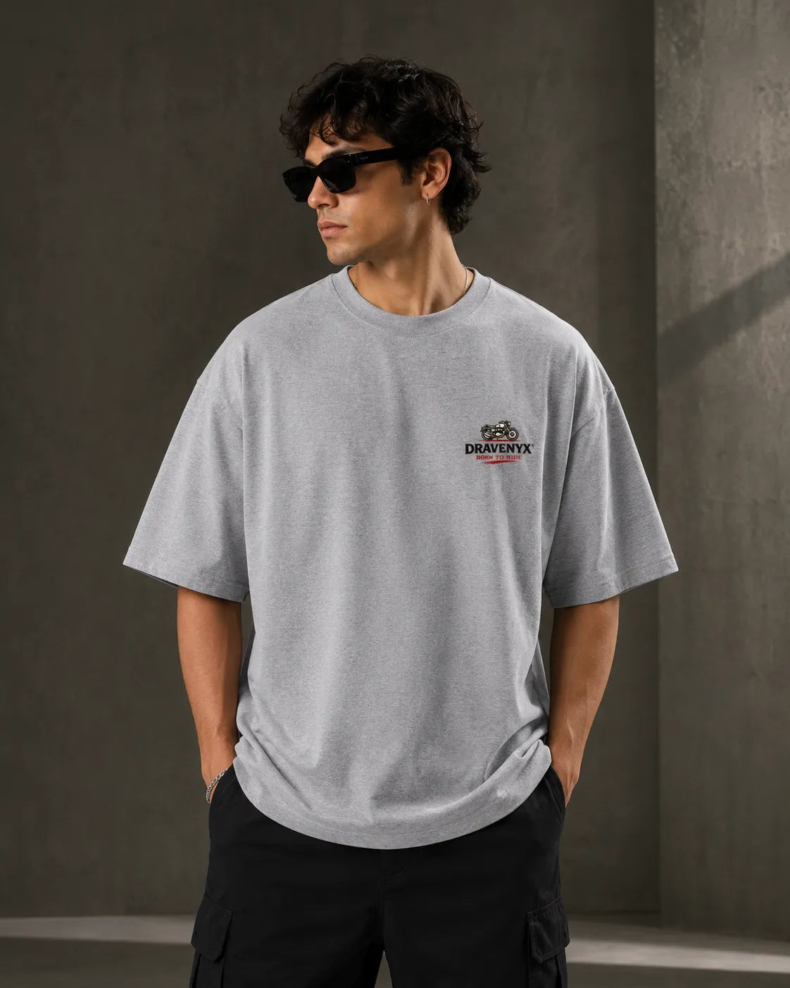 DRAVENYX® Born To Ride oversized tee in Grey Melange — front view showing left chest moto-badge print and drop-shoulder silhouette — back view with full-panel moto-art graphic and 'Born To Ride / Built For Freedom' DTF print