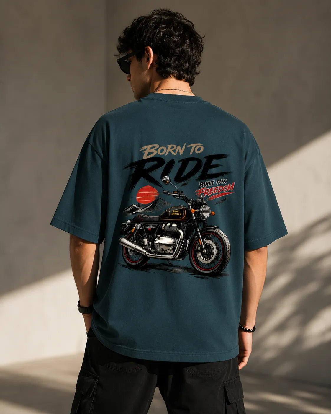 DRAVENYX® Born To Ride oversized tee in Petrol Blue — front view showing left chest moto-badge print and drop-shoulder silhouette — back view with full-panel moto-art graphic and 'Born To Ride / Built For Freedom' DTF print